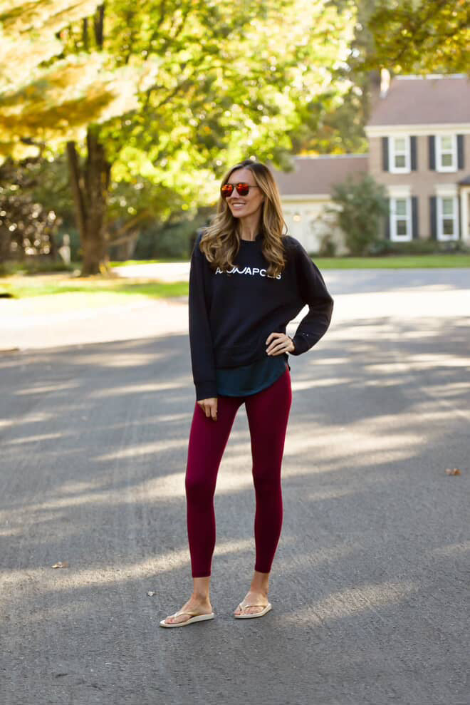 Woman in  navy sweatshirt with 'ANNAPOLIS' and red leggings standing on a street with trees and a house in the background