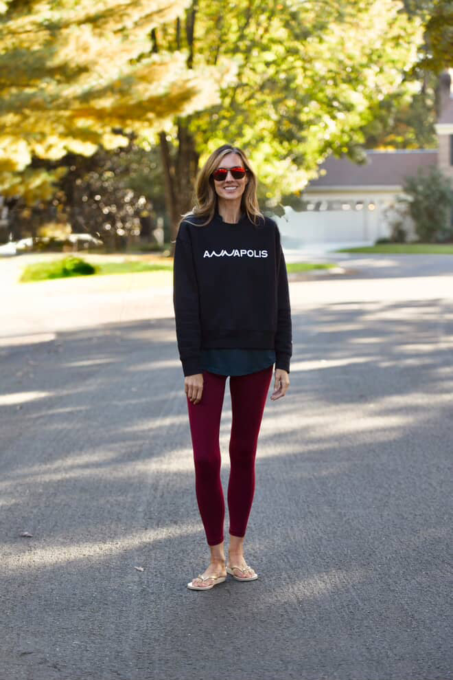 Woman wearing a navy sweatshirt with 'ANNAPOLIS' text and red leggings standing on a street.