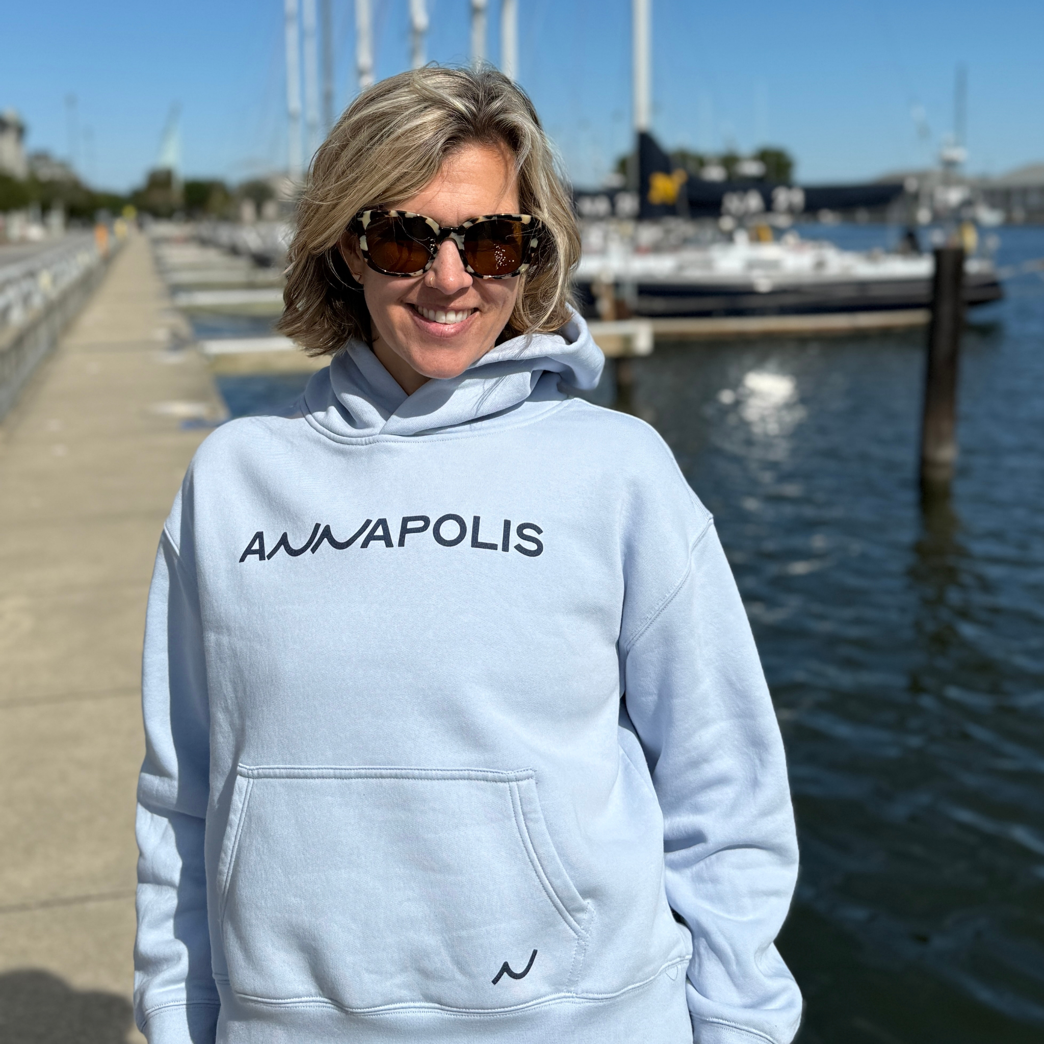 Person wearing a light blue hoodie with 'ANWAPOLIS' text, standing by a waterfront.