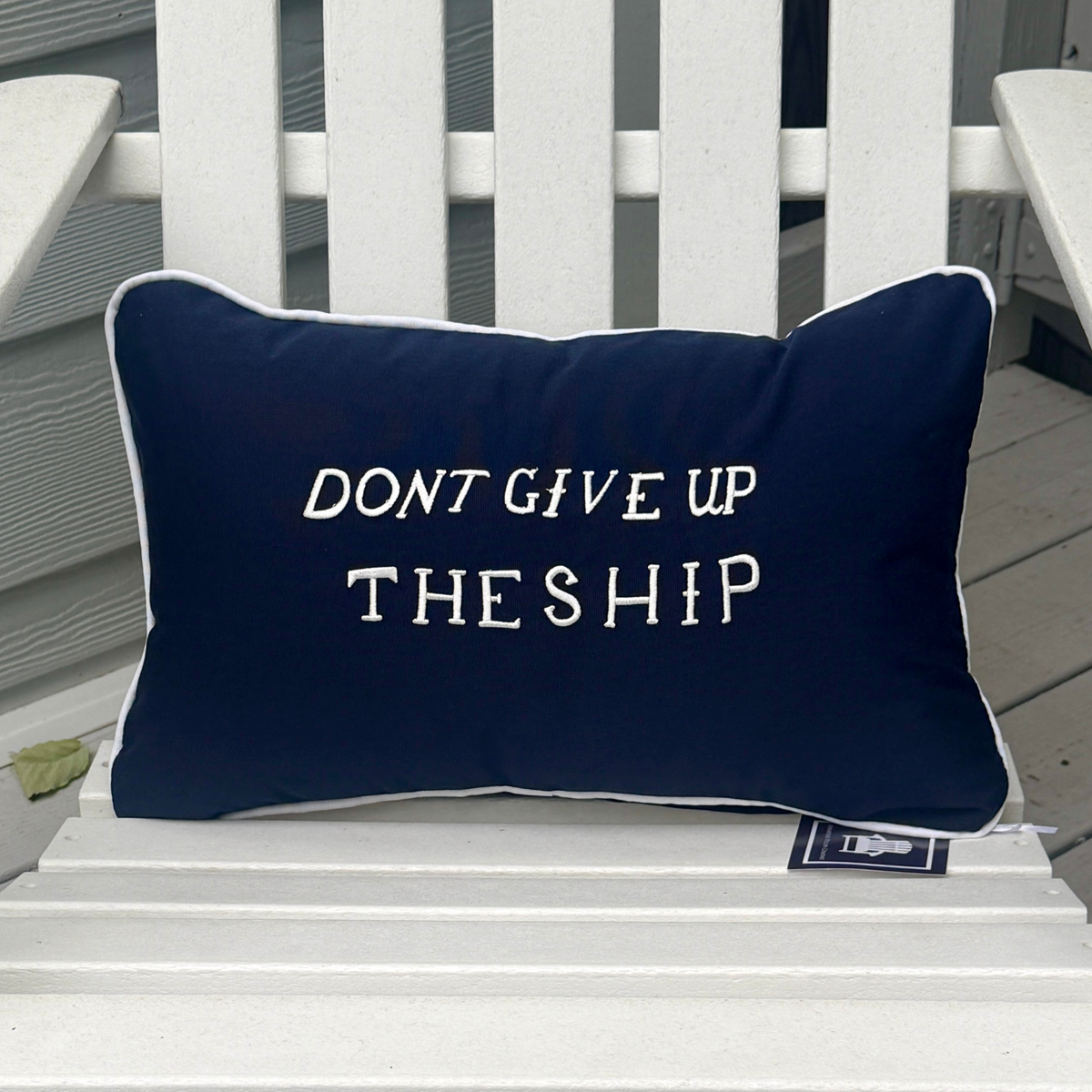 Navy Don’t Give Up the Ship lumbar pillow with white embroidery and piping on a white Adirondack chair.